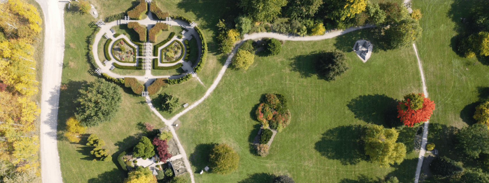 An aerial view looking at pathways and gardens in The Arboretum. The English Garden can be seen as it forms an oval surrounded by shrubs. A road follows the left side of the image.