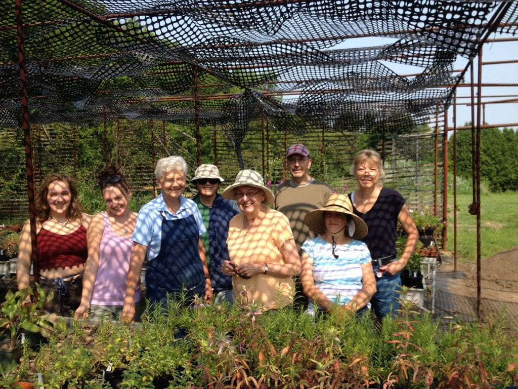  A group of volunteers pose for a picture behind a table of plants.